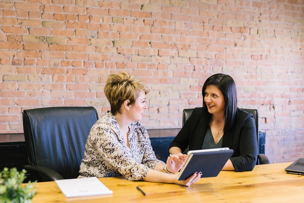 Two professional chat, side-by-side, in an office.